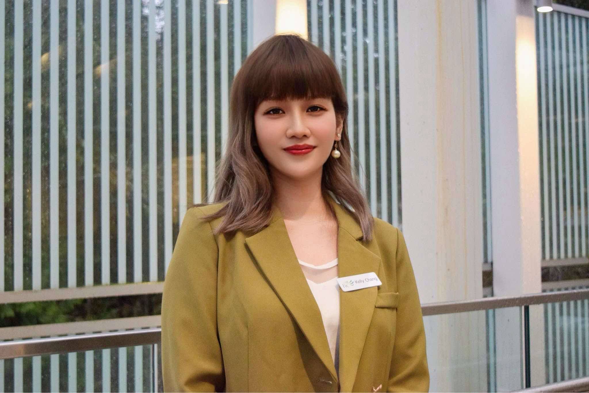 Portraits of a female counsellor with brown hair and bangs wearing an olive green blazer over a white top stands outside.