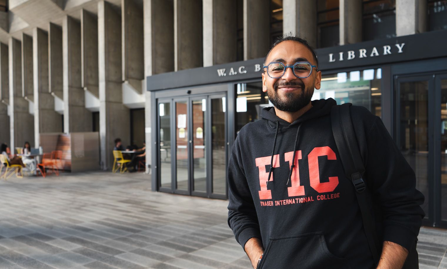 Student smiling wearing a black FIC hoodie standing on the right side of the frame.